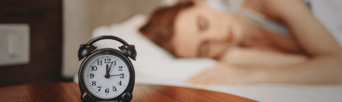 blurry image of a girl sleeping peacefully in the background, with a focused alarm clock in the foreground, symbolizing the connection between rest and mental health