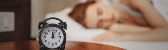 blurry image of a girl sleeping peacefully in the background, with a focused alarm clock in the foreground, symbolizing the connection between rest and mental health