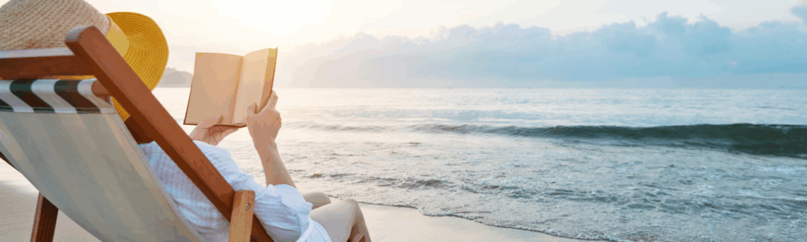 Person reading alone on a quiet beach, symbolizing summer reflection and self-care.
