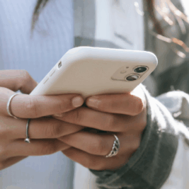 Close-up of a woman's hands holding an iPhone, displaying a blog titled 'Digital Wellness: Finding Balance in Our Always-Connected World' on the screen, emphasizing mindfulness in technology use.