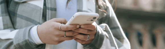 Close-up of a woman's hands holding an iPhone, displaying a blog titled 'Digital Wellness: Finding Balance in Our Always-Connected World' on the screen, emphasizing mindfulness in technology use.